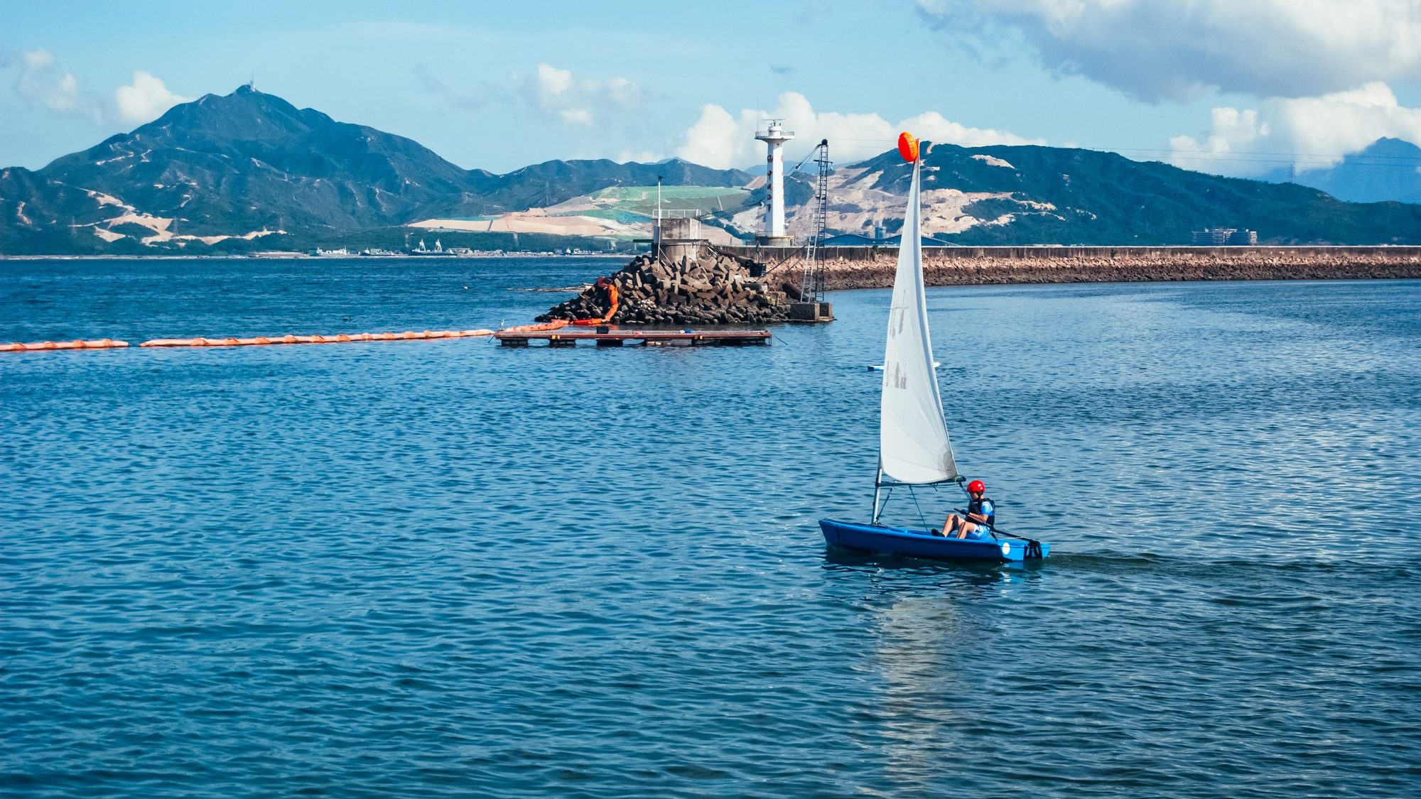 A sailing boat passing a coastal lighthouse